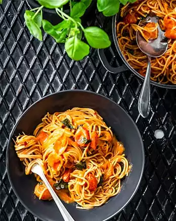 Der Schriftzug „Pasta” auf einem Foto von einem Pastagericht mit Tomatensauce auf einem Teller.